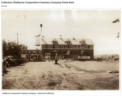 Black and white image of a two-story building with chimney and water tower behind on the left.  An old-style gas pump is in front of the building and cars are parked to the left.  A man walks out of the frame on the left. 
Shelburne cooperative Creamery Company - Parke Kent Collection.