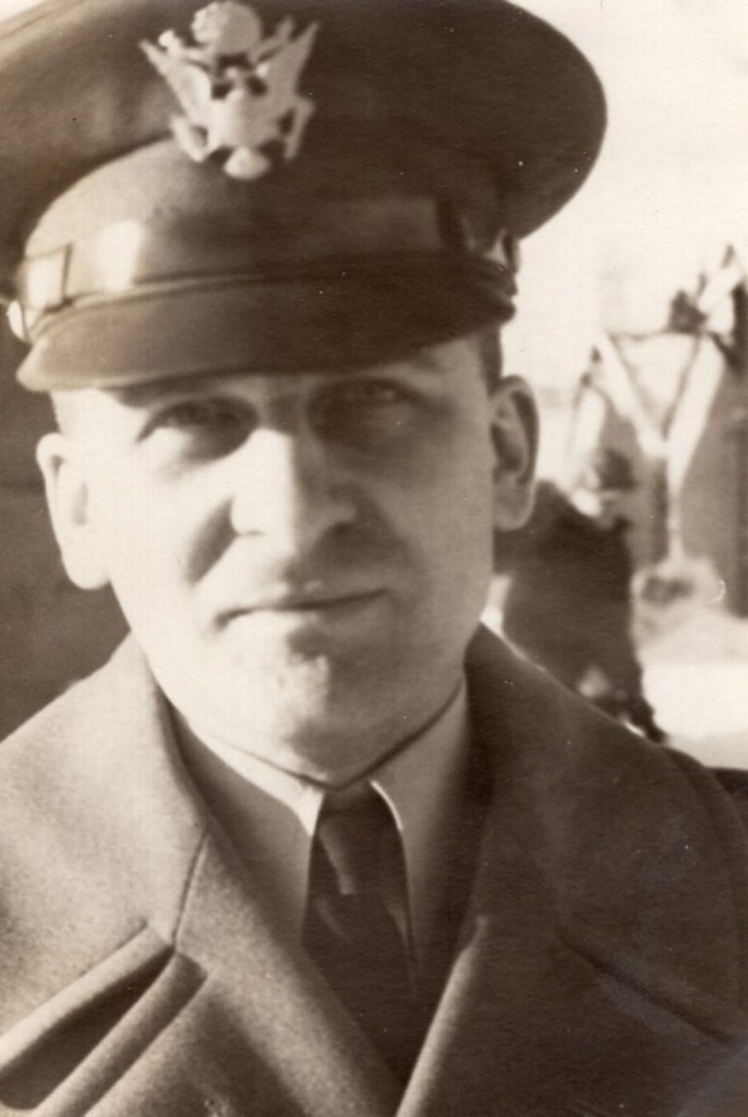 Black and white, three-quarters image of a man in military uniform looking at the viewer.  His coat has a thick collar, and his hat has an eagle emblem.